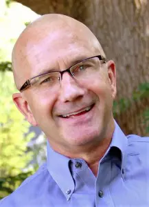 A man with glasses and bald head smiling.
